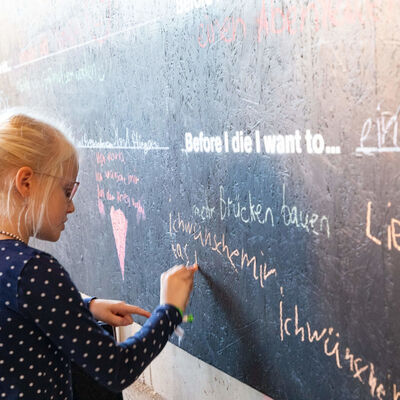 Ein Mädchen schreibt mit Kreise ihre Wünsche auf eine Tafel.