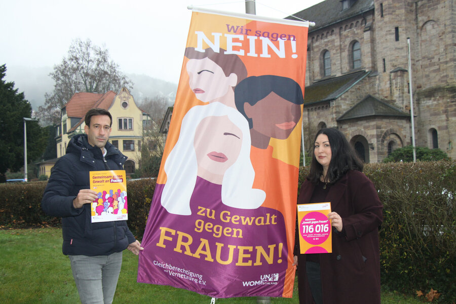 B�rgermeister Tobias Dannenberg und die Gleichstellungsbeauftragte Melissa Castillo halten die zum "Orange Day" gehisste Flagge auseinander und zeigen entsprechende Flyer in die Kamera.