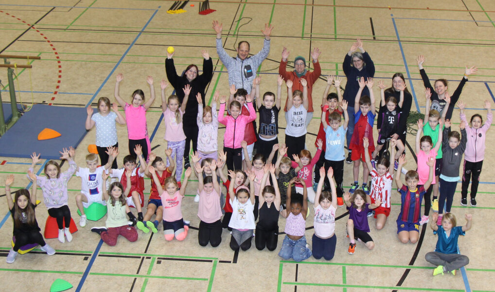 Aus der Giraffenperspektive aufgenommenes Foto einer Kindergruppe in Turnbekleidung innerhalb einer Sporthalle.
