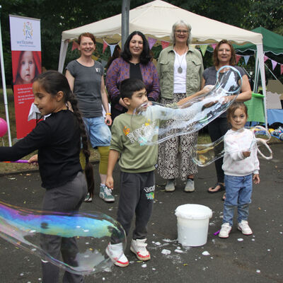 (Hinten, v.li.) Martina Betjen vom Caf&eacute; Kinderwagen des Mehrgenerationenhauses, Melissa Castillo, Gleichstellungsbeauftragte der Stadt Hann. M&uuml;nden, Antje Steinborn vom Netzwerk Fr&uuml;he Hilfen Tina Krause vom Familienzentrum schauen (vorne, v.li.) Lavin, Lauend und Barin zu, die Riesenseifenblasen erschaffen.